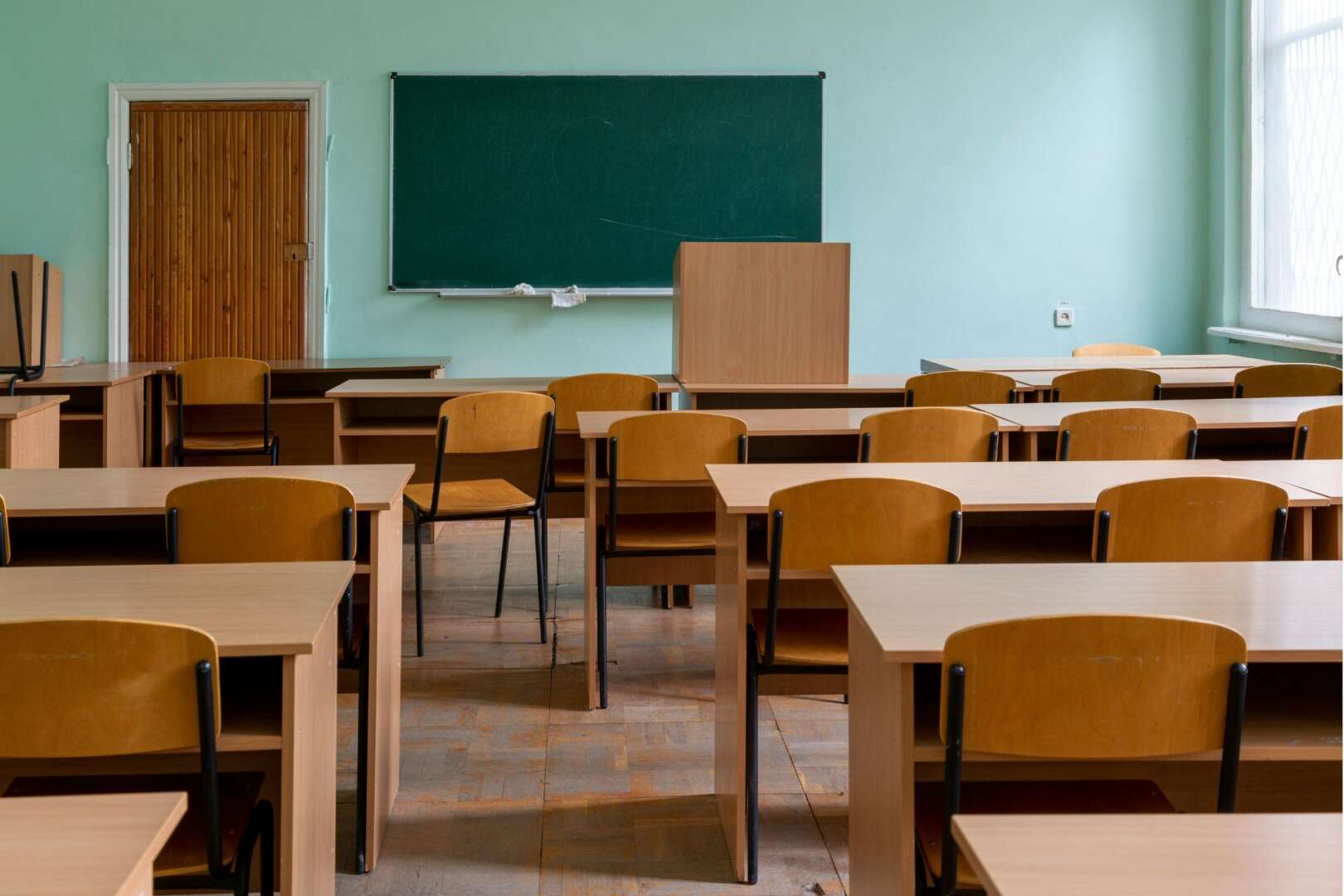 Empty classroom with rows of wooden desks and chairs facing a chalkboard