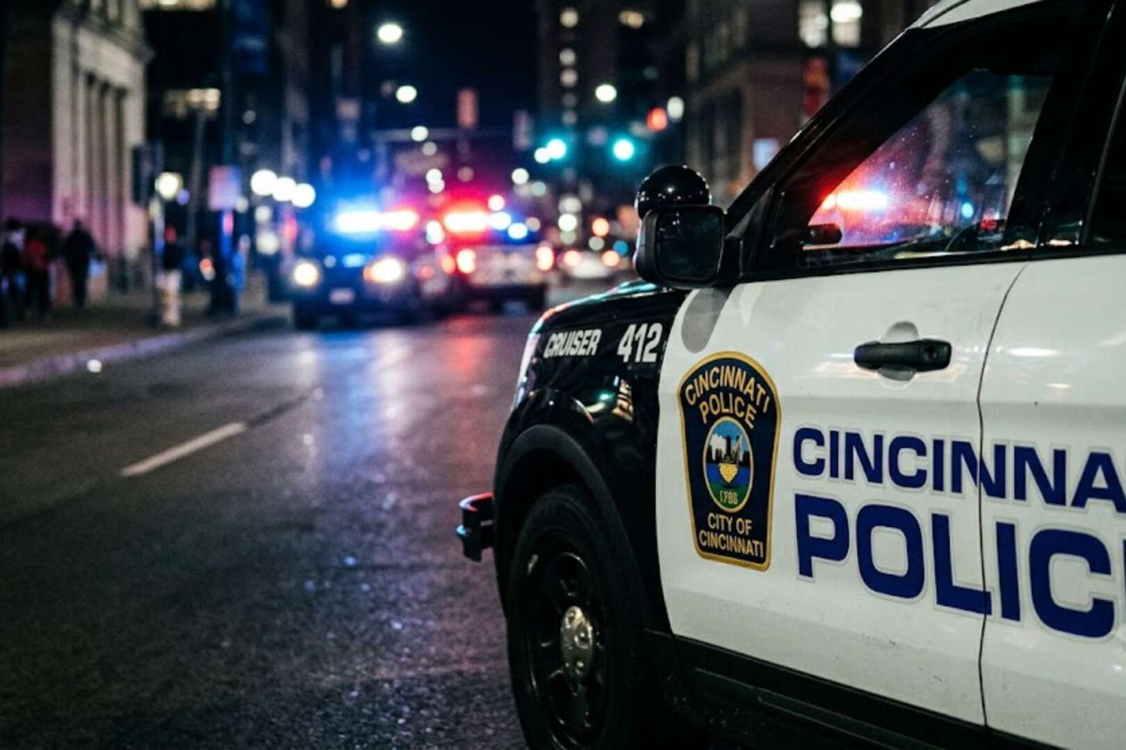 Close-up of the side of a Cincinnati Police cruiser with emergency lights flashing at a city street scene at night.