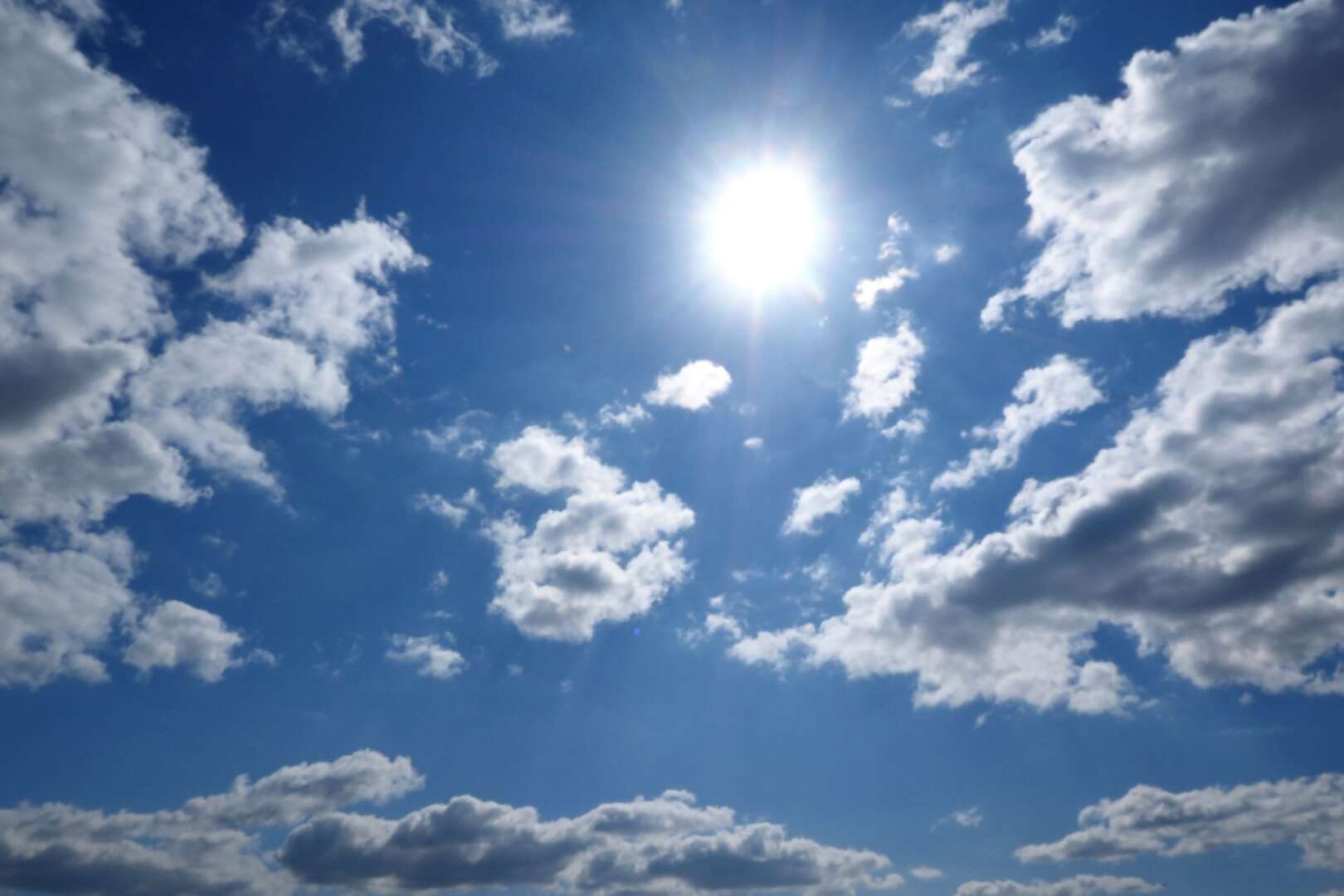 Bright sun shining through scattered white clouds in a blue sky