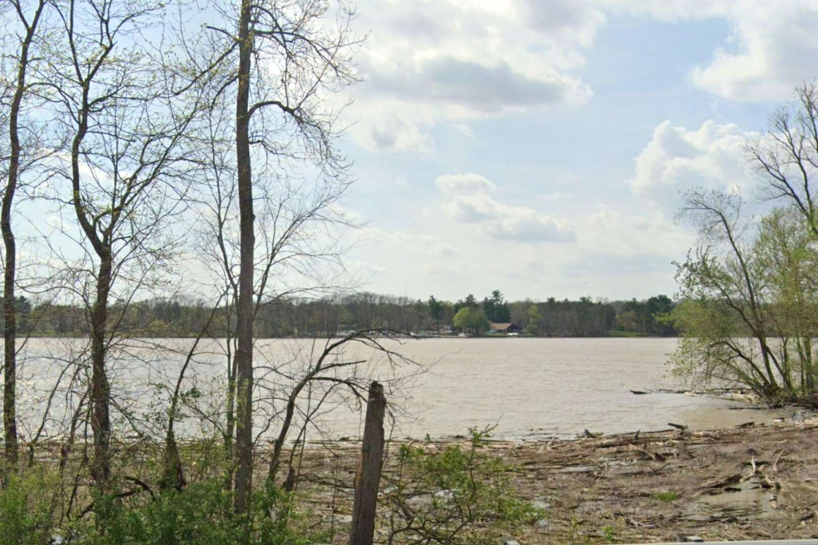 Wide view of the Scioto River on a partly cloudy day, seen through trees along the riverbank.