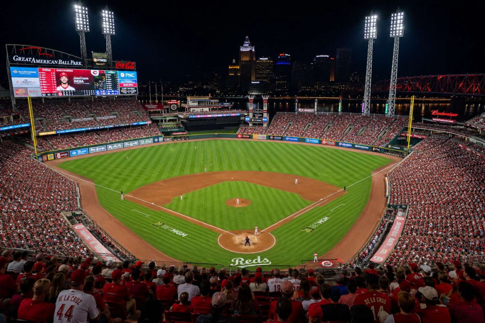 A wide-angle night view of a fully lit, packed baseball stadium during the Cincinnati Reds vs. Chicago Cubs series, showing the field and packed stands.