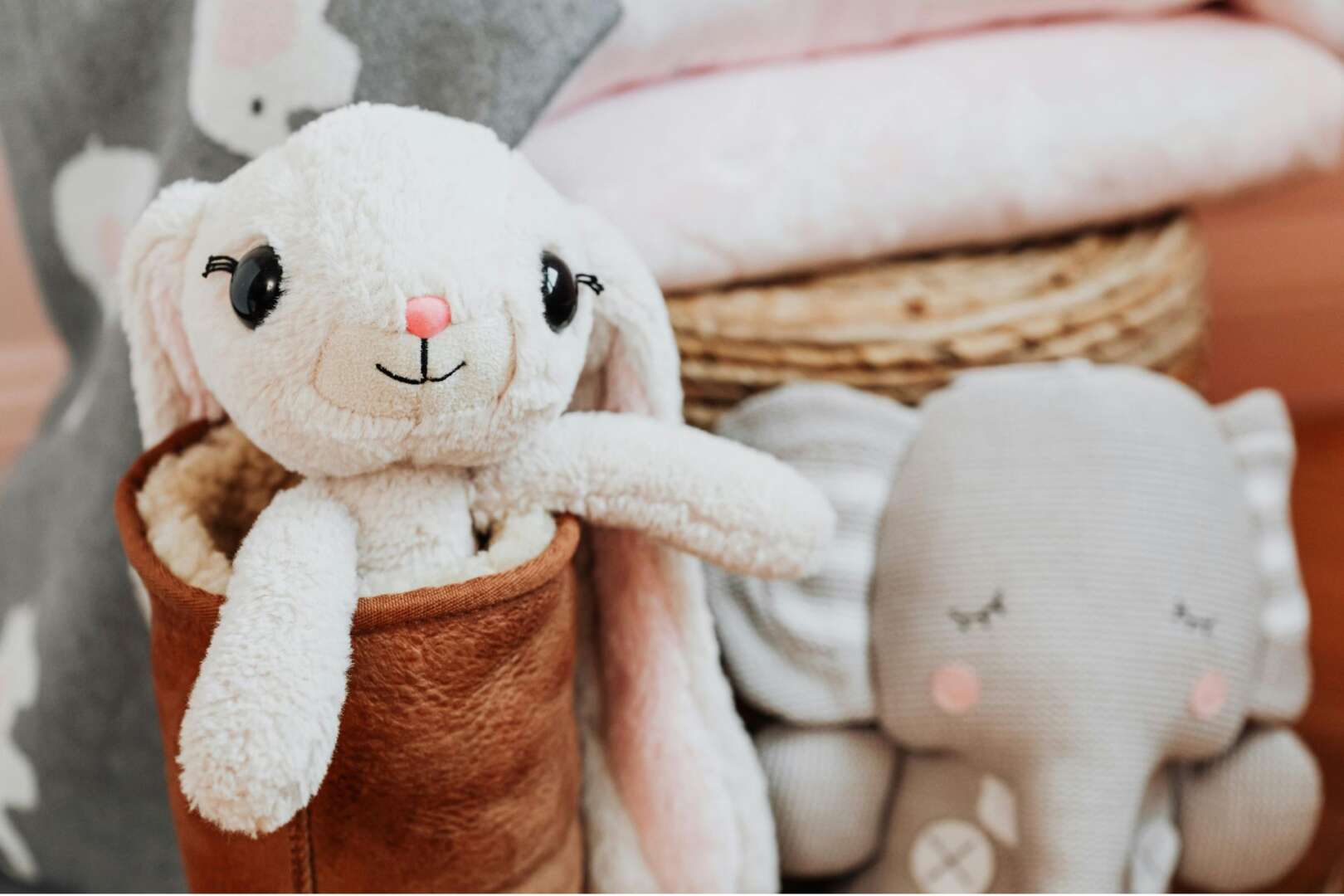 A soft white plush bunny sitting in a small brown basket next to a plush gray elephant, displayed for the Cincinnati Zoo stuffed animal clinic.
