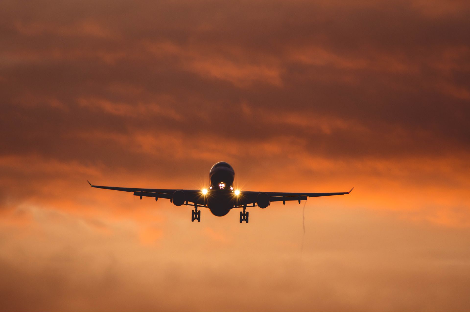 Commercial passenger airplane flying directly toward the camera through dramatic golden-orange sunset clouds.