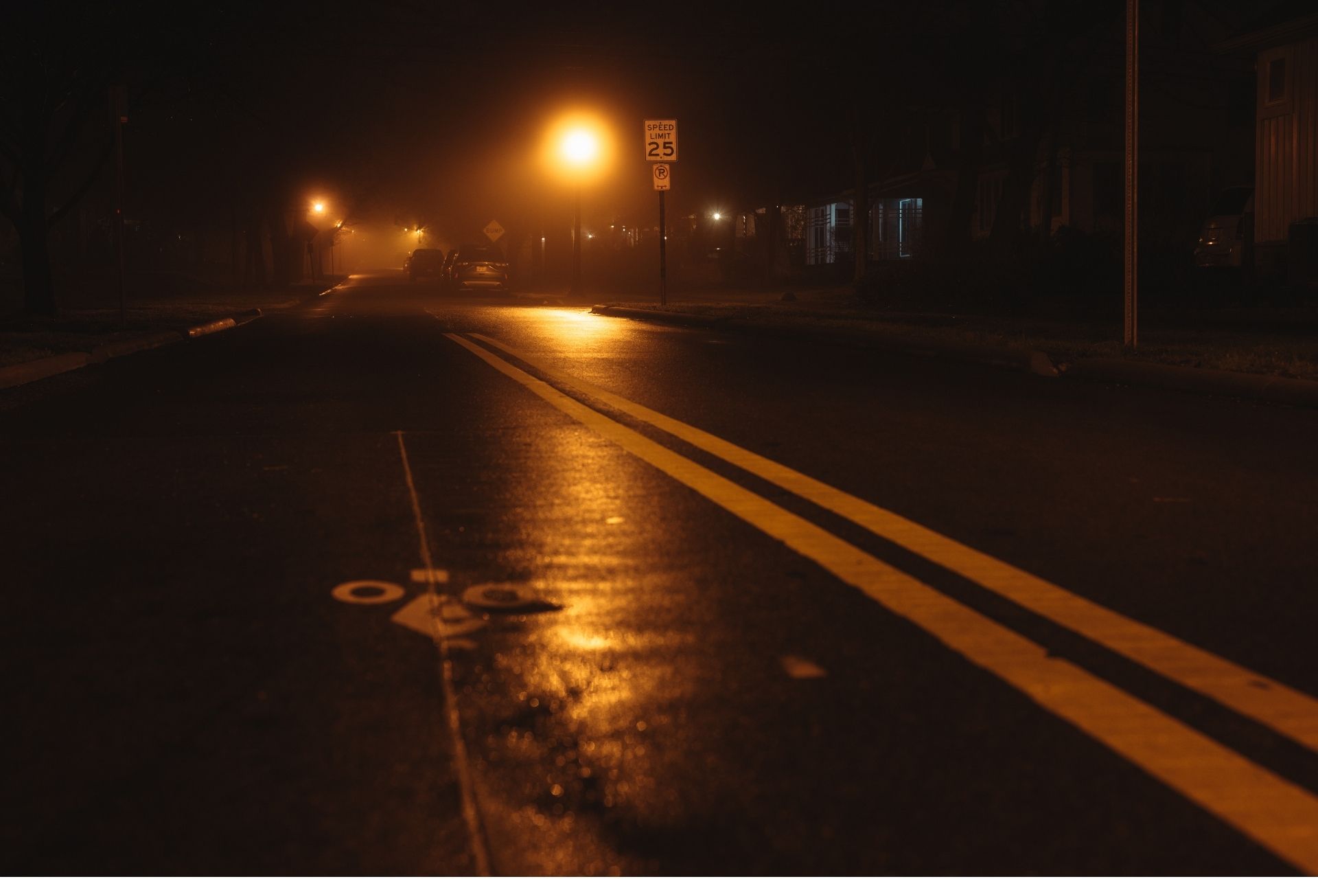 An empty, rain-slicked city road at night illuminated by warm streetlights, depicting a quiet street under curfew.