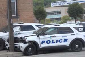 Two damaged Cincinnati police cruisers, including a K9 unit vehicle, parked outside a police facility.