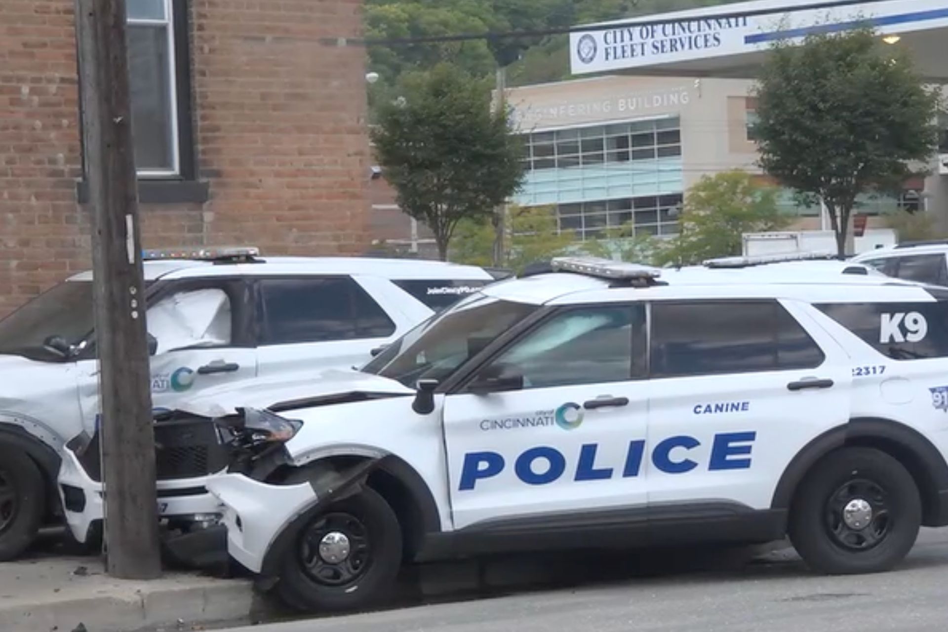 Two damaged Cincinnati police cruisers, including a K9 unit vehicle, parked outside a police facility.
