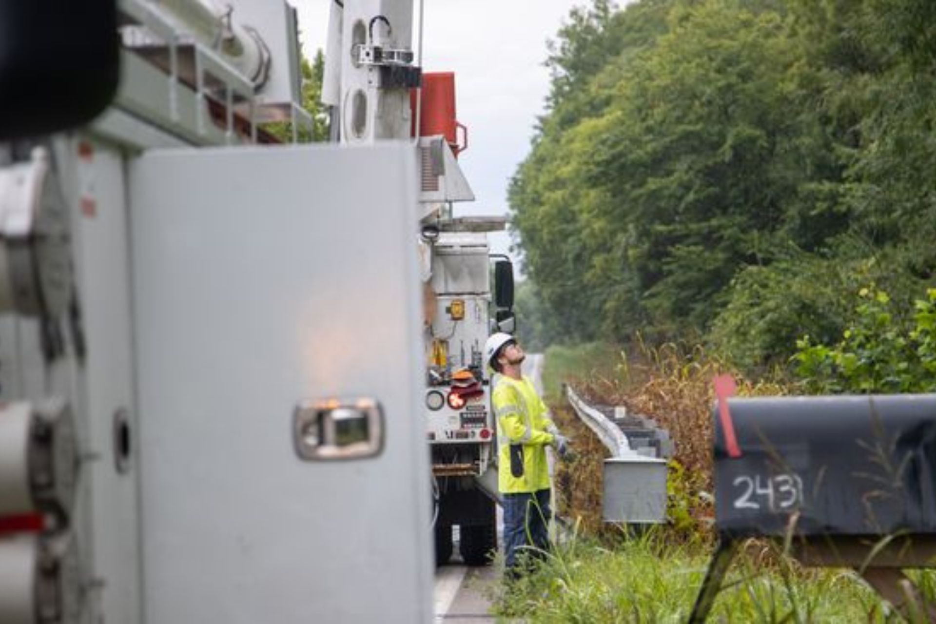 Duke Energy utility worker standing next to a bucket truck on a tree-lined road in Cincinnati during power restoration efforts following a derecho.