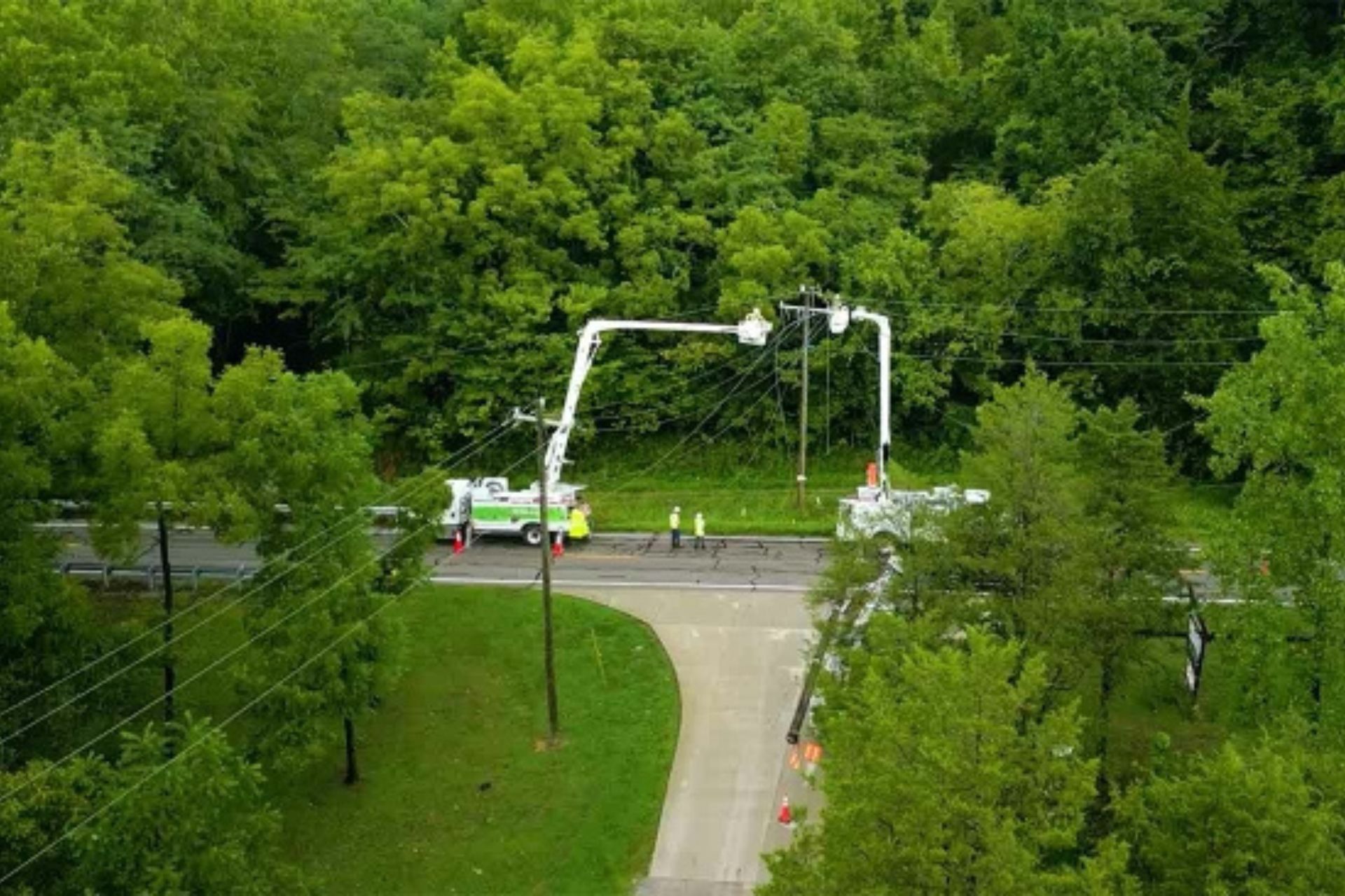 Aerial view of Duke Energy utility trucks repairing power lines along a wooded road in Cincinnati.