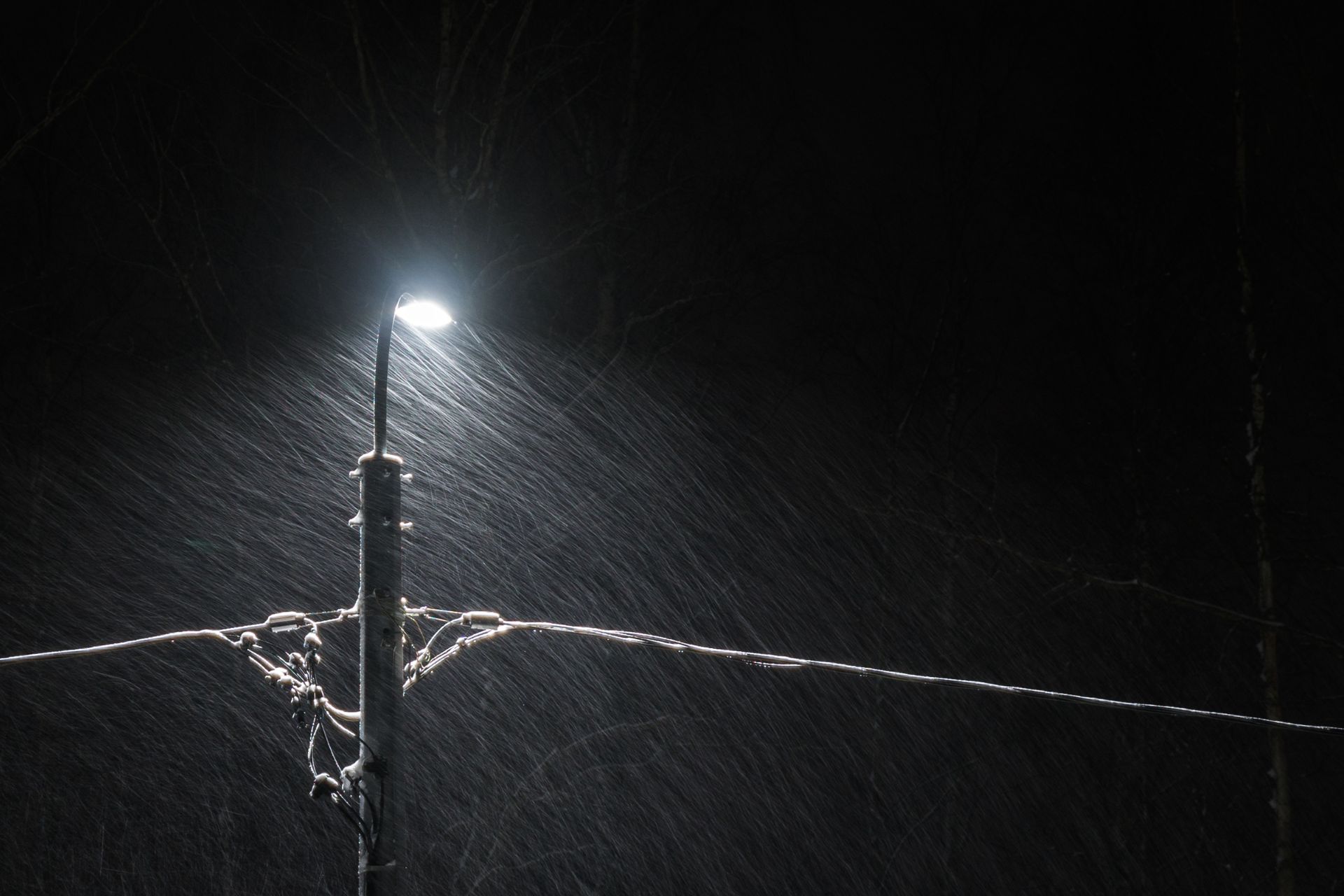 A street light illuminating heavy, torrential rainfall at night along overhead utility power lines during a severe storm.