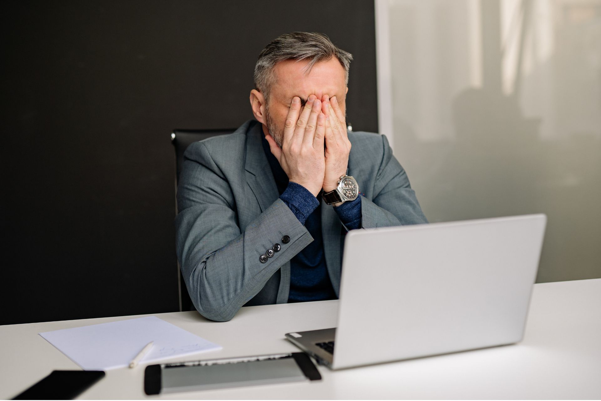 Frustrated businessman sitting at a desk with his head in his hands in front of a open laptop.