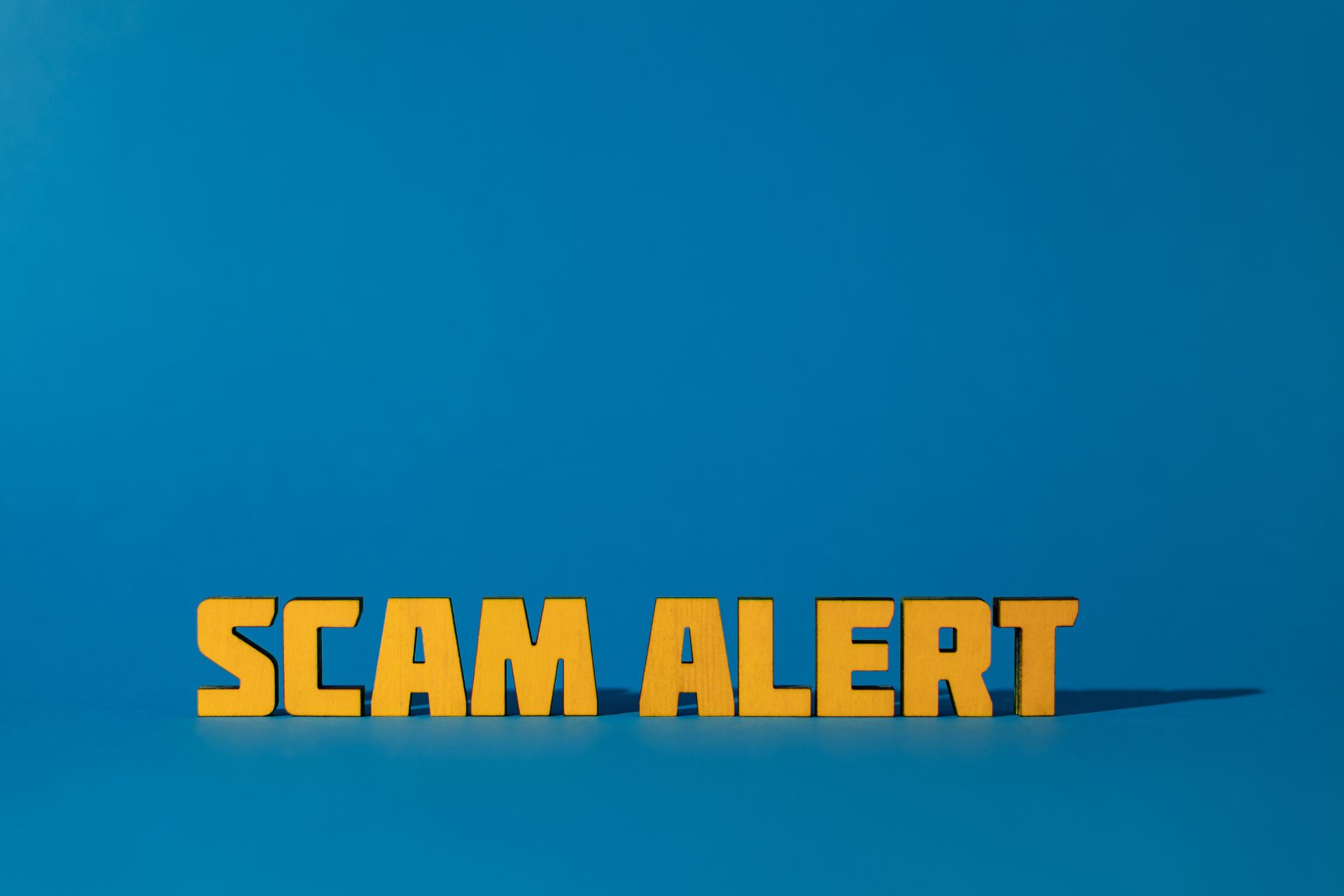 Graphic featuring bold yellow text reading "SCAM ALERT" on a solid blue background.