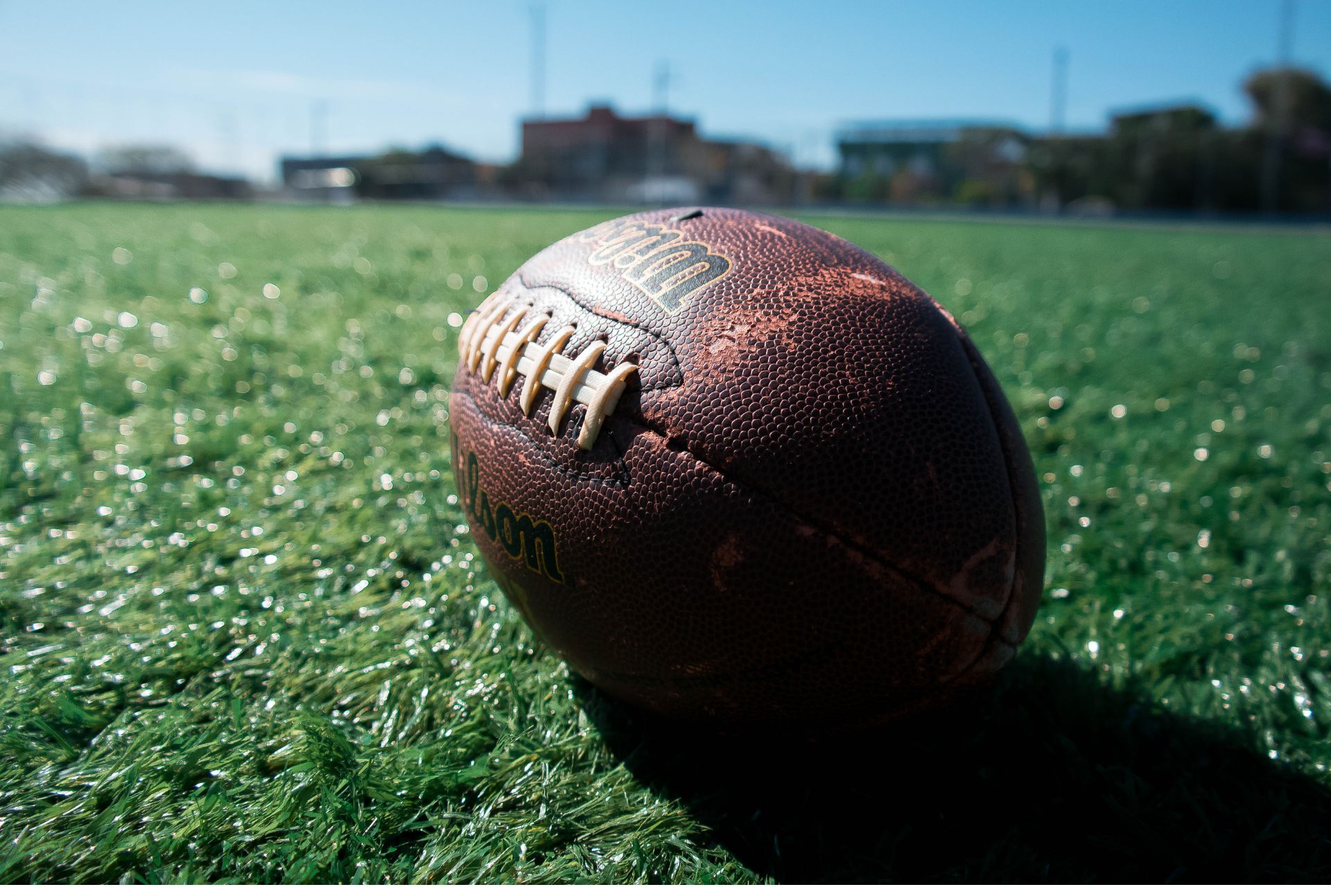 An American football resting on a green turf field.