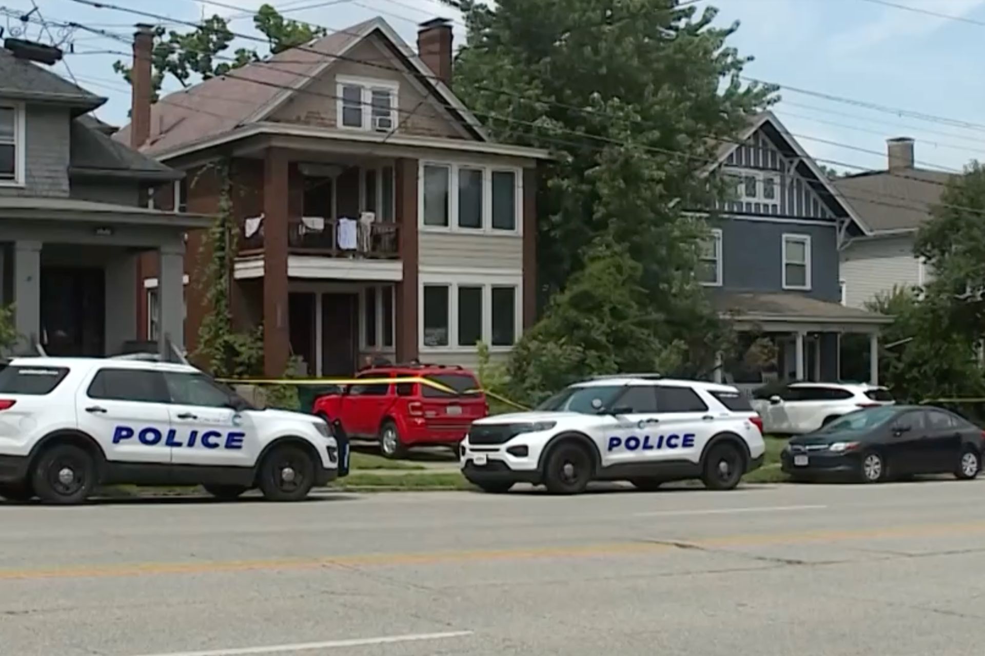 Police vehicles parked on a residential street in front of multi-story houses.