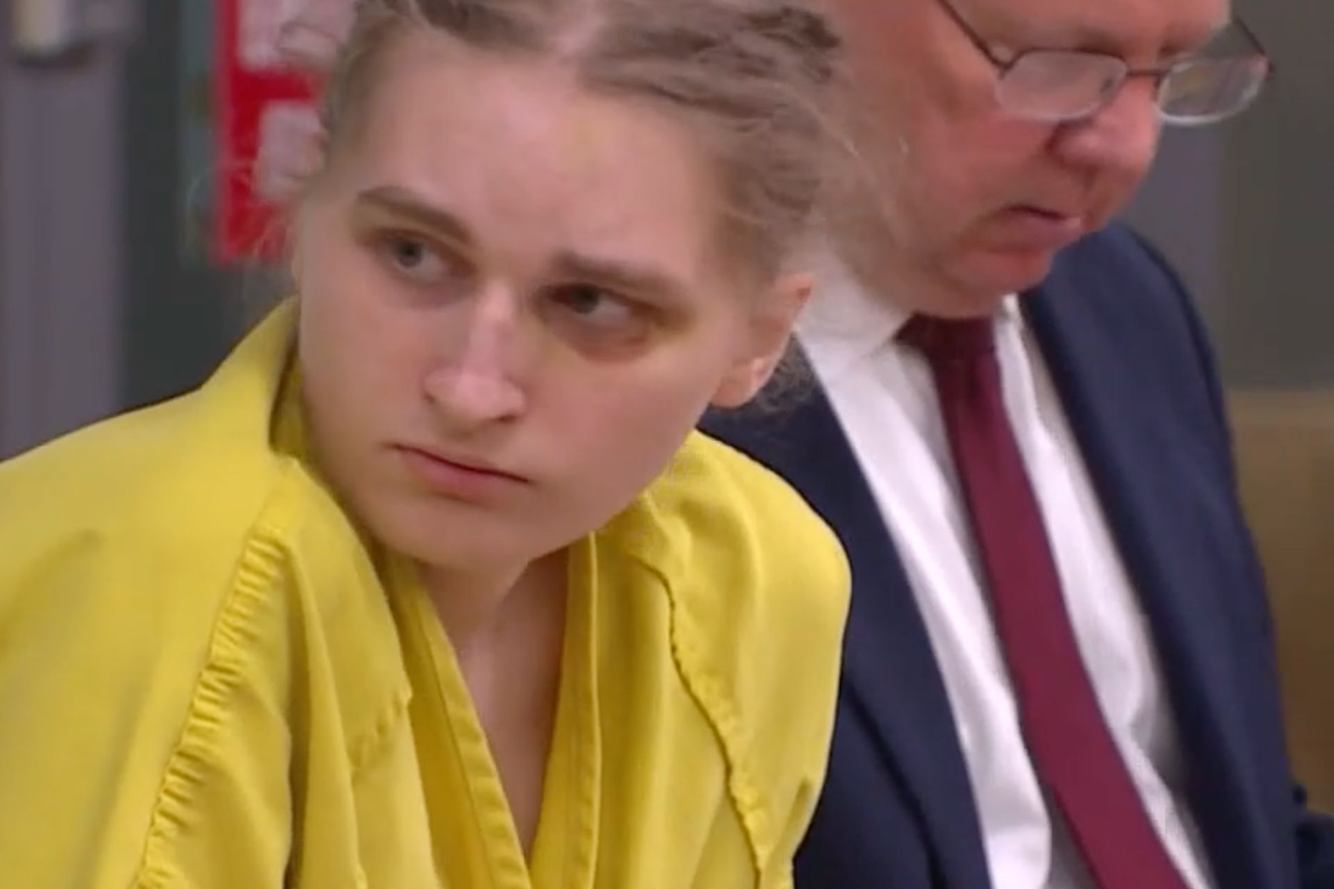 Young woman in a yellow jumpsuit appearing in court alongside an attorney.