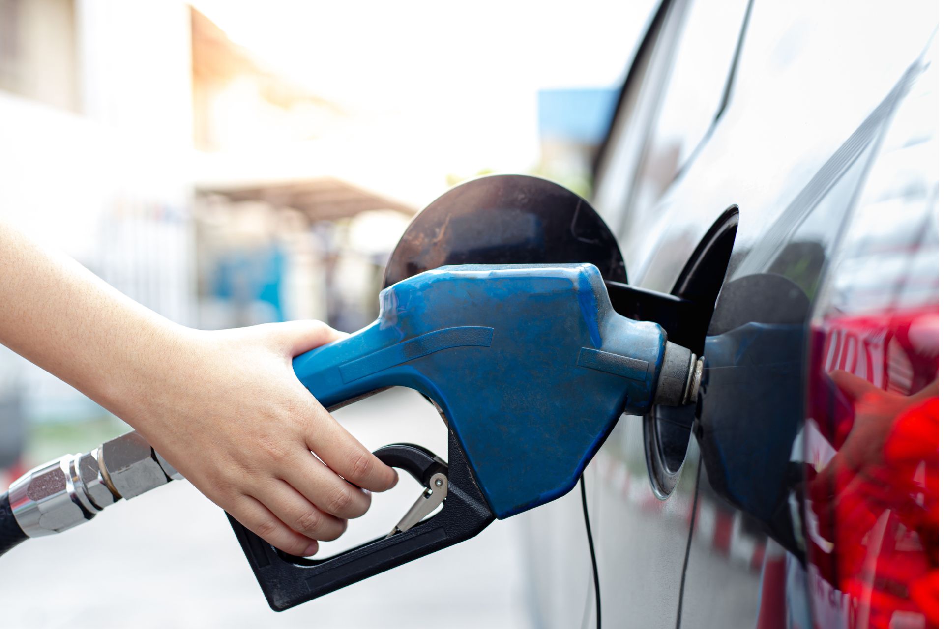 Person holding a blue gas pump nozzle while refueling a vehicle.