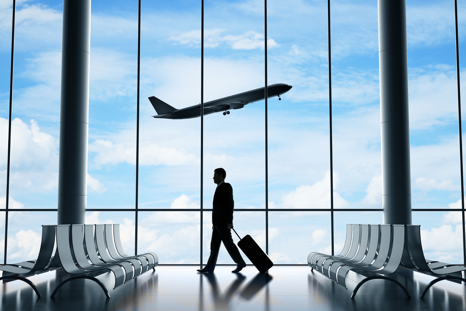 Silhouette of a traveler with rolling luggage walking through an airport terminal as an airplane takes off outside.