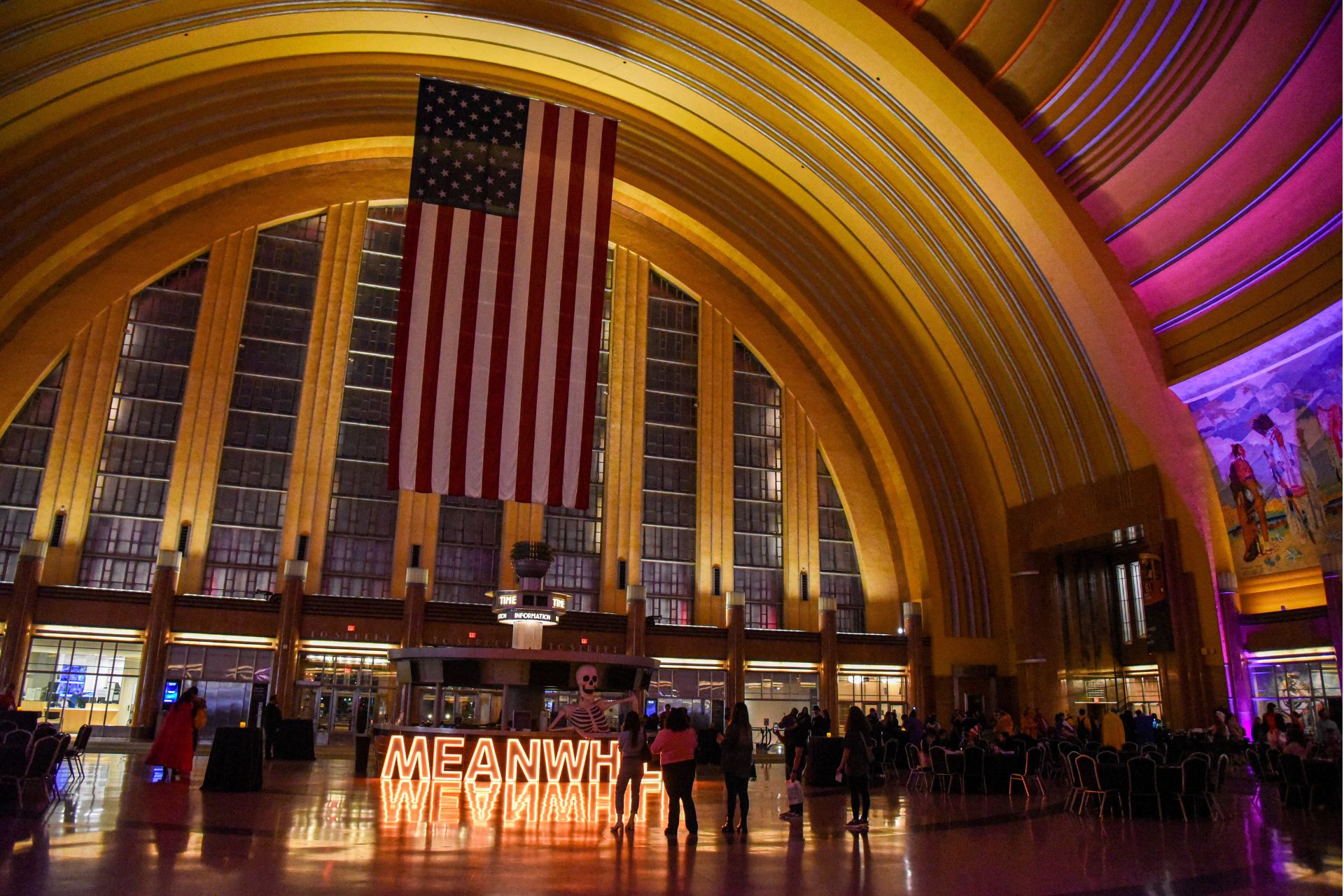 Cincinnati Museum Center grand rotunda illuminated with purple and warm lighting for a Halloween after-hours event, with a large American flag hanging in the center.
