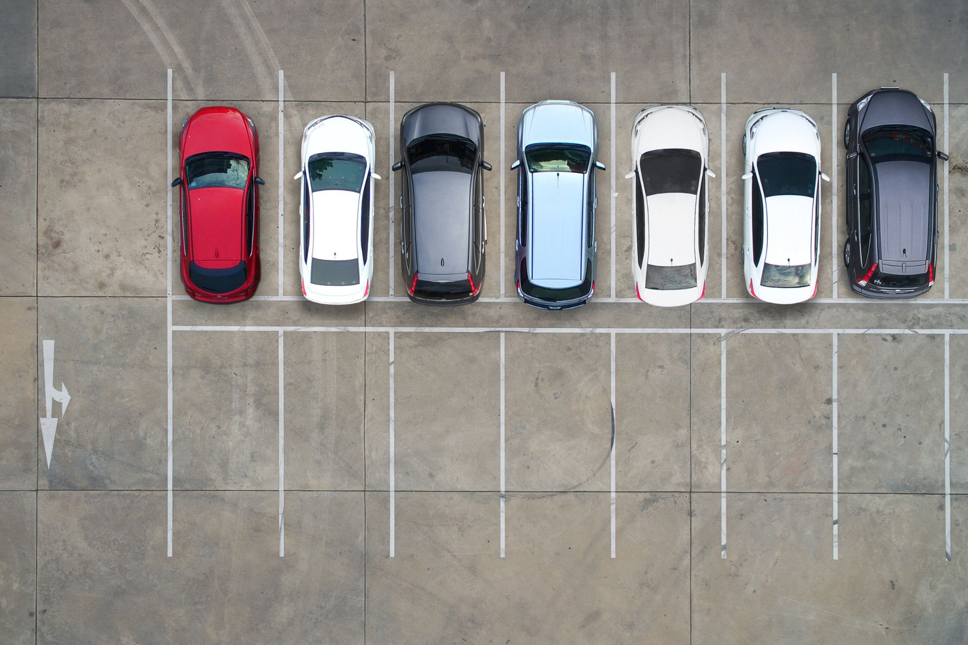 Aerial view of seven cars neatly parked in a row in a paved parking lot
