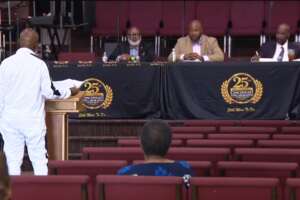 Speaker in a white suit presenting before a panel seated at a dais during a public review of Cincinnati police stop data.