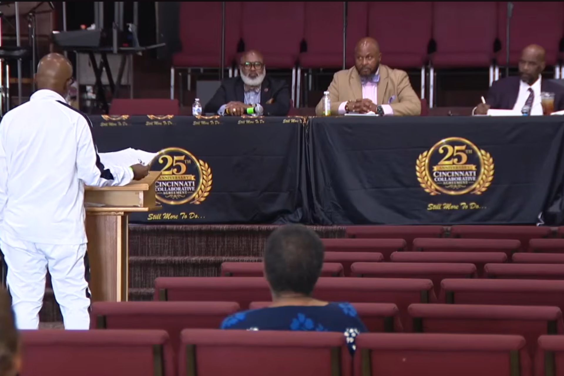 Speaker in a white suit presenting before a panel seated at a dais during a public review of Cincinnati police stop data.