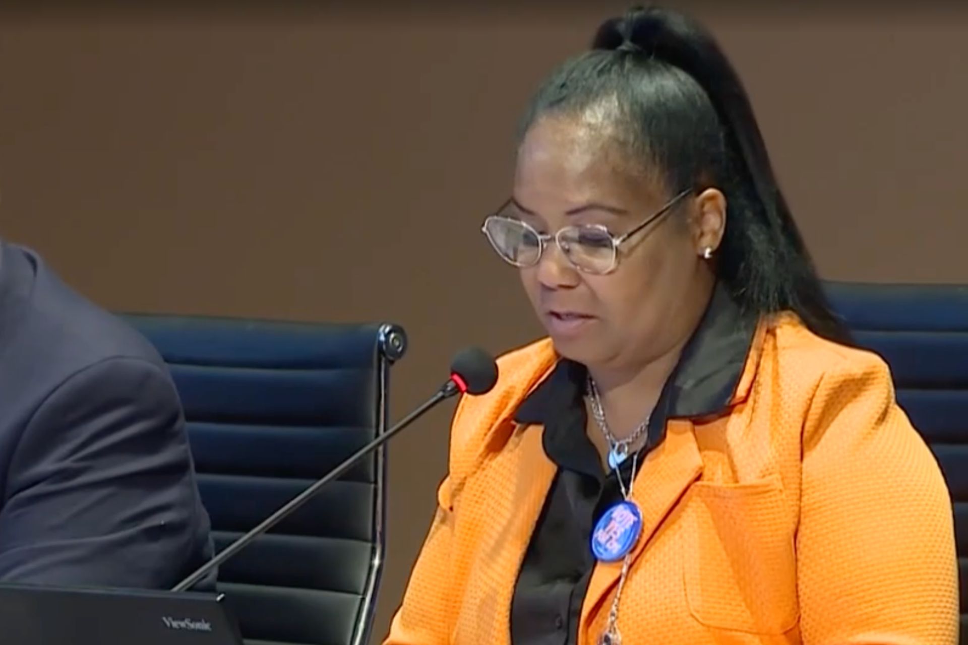 A screenshot of CPS Superintendent Shauna Murphy in an orange suit, in front of a microphone, sitting during a press briefing regarding the latest result of the report card rating.