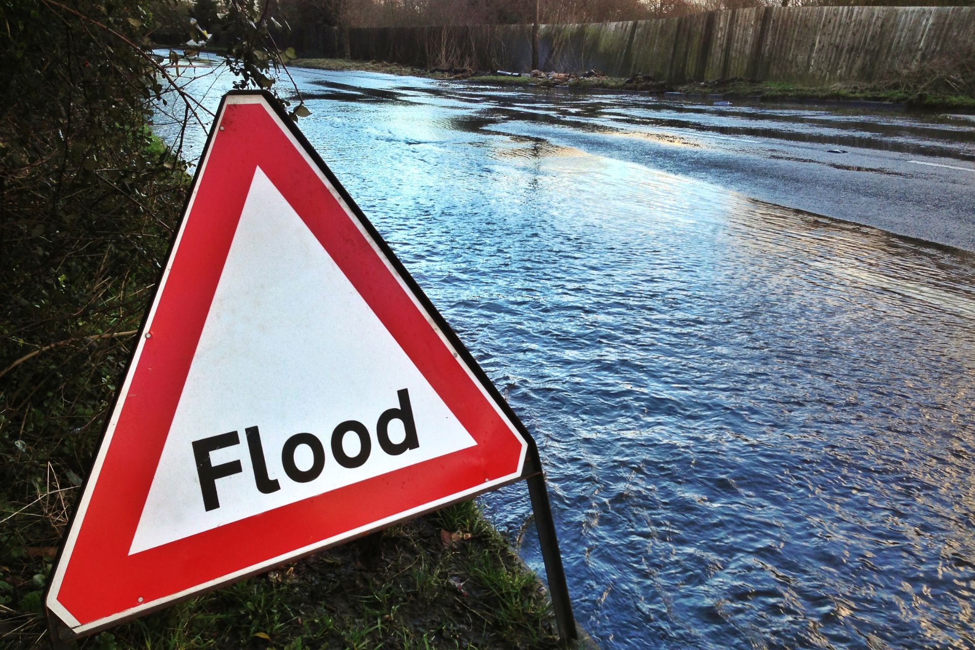 A red and white triangular warning sign reading "Flood" next to rising water.