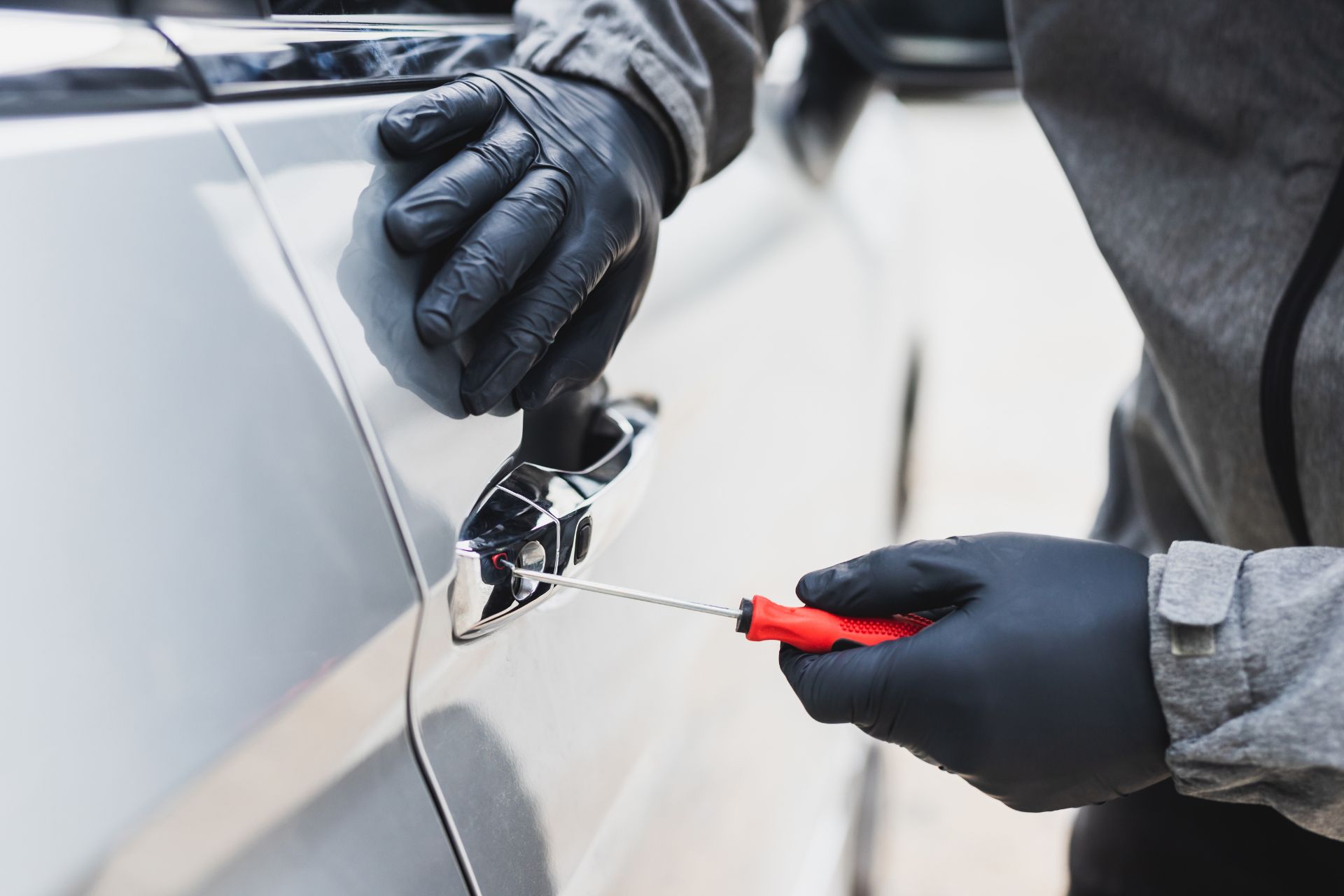 erson wearing black gloves using a tool to pick a car door lock.