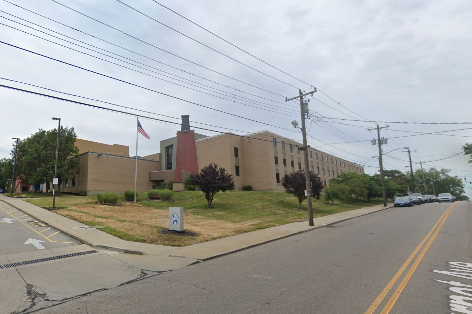 Exterior view of a multi-story, brick Cincinnati Public Schools building with a flagpole, seen from the street intersection.