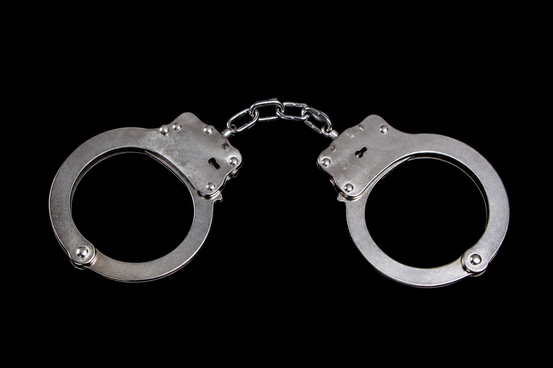 A pair of shiny silver metal handcuffs against a black background.