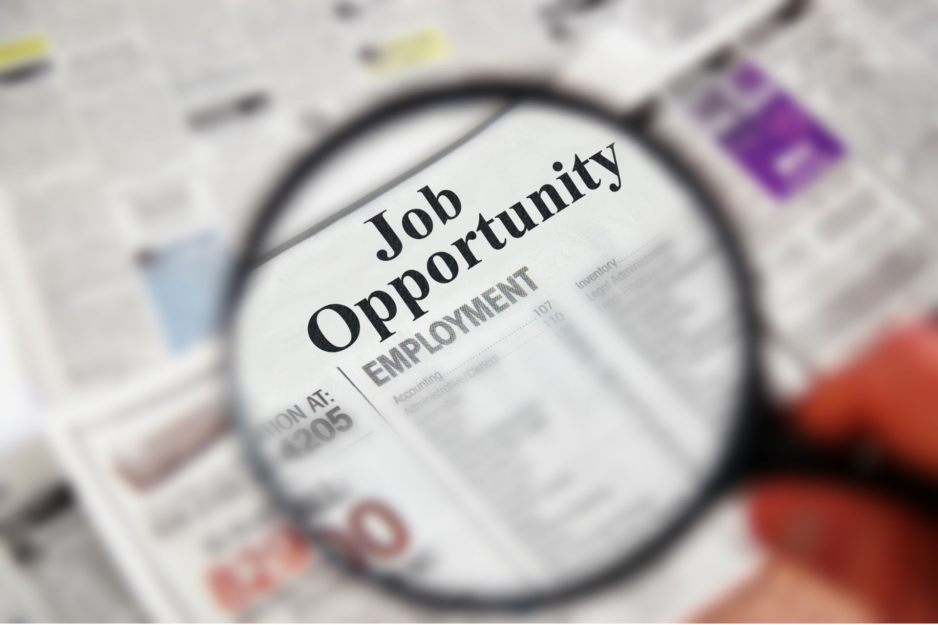 Magnifying glass focused on a "Job Opportunity" listing in a classified newspaper section.