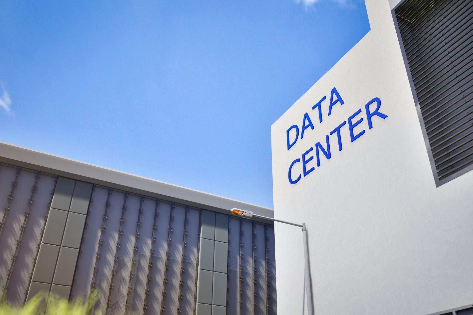 White data center building with large blue “DATA CENTER” lettering on its exterior wall, photographed from below against a blue sky