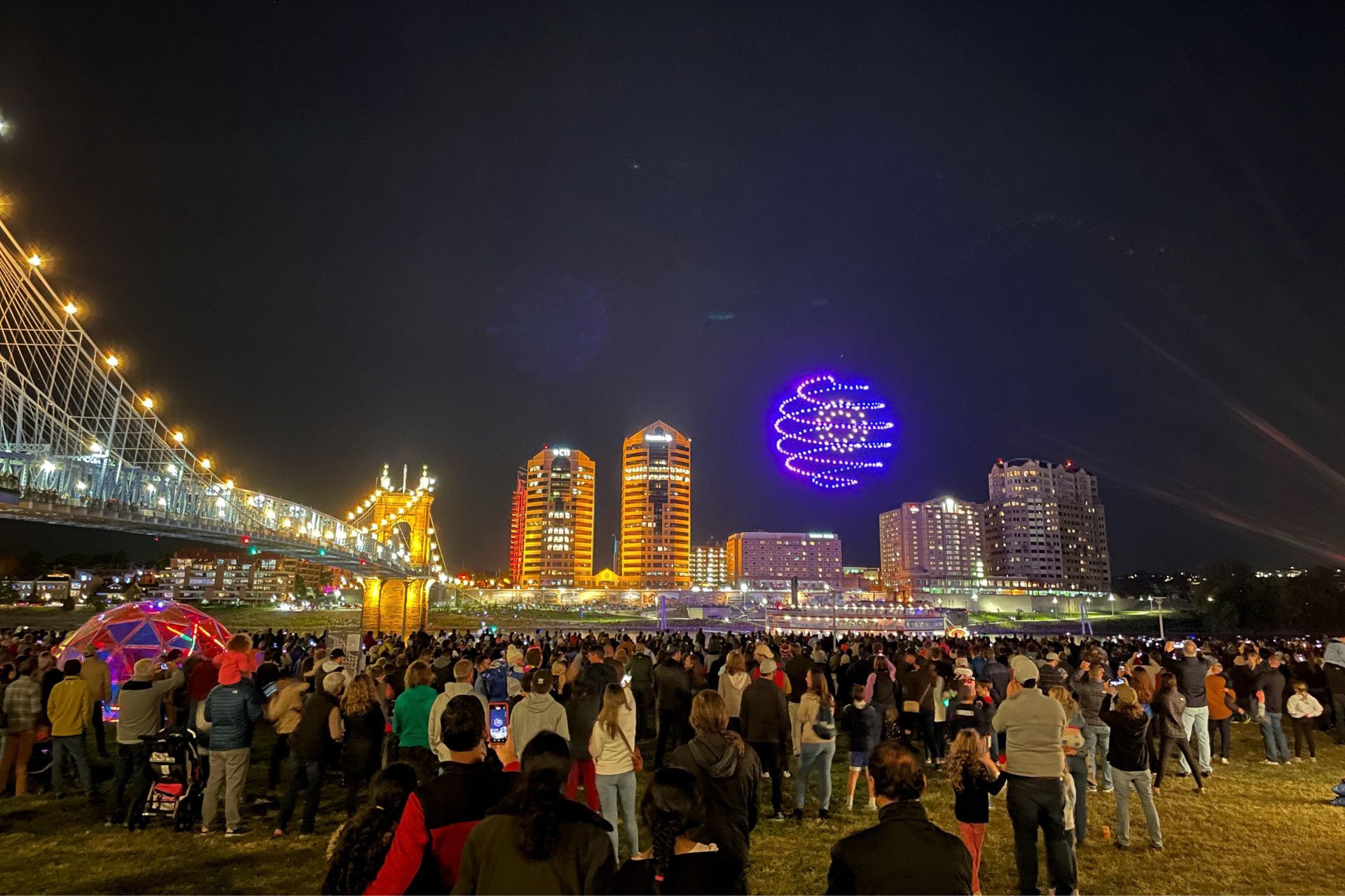 Large crowd gathered outdoors at night viewing illuminated buildings, bridge, and light projections during BLINK Cincinnati