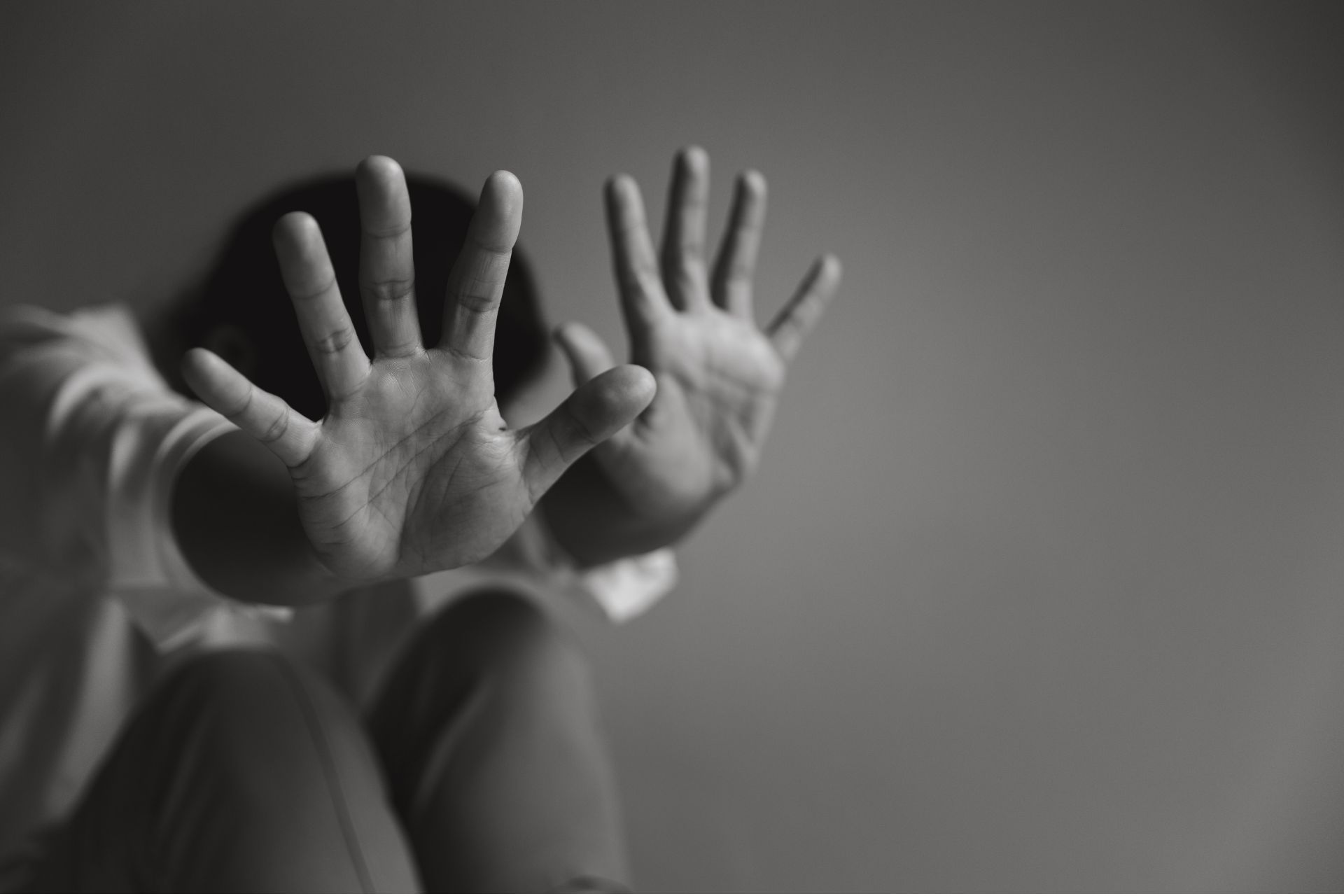 Person in shadow crouching with their hands raised defensively in front of their face.