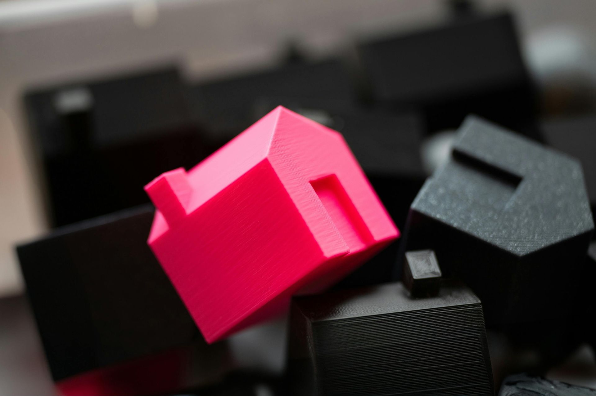 A single bright pink miniature house standing out among several black miniature houses.