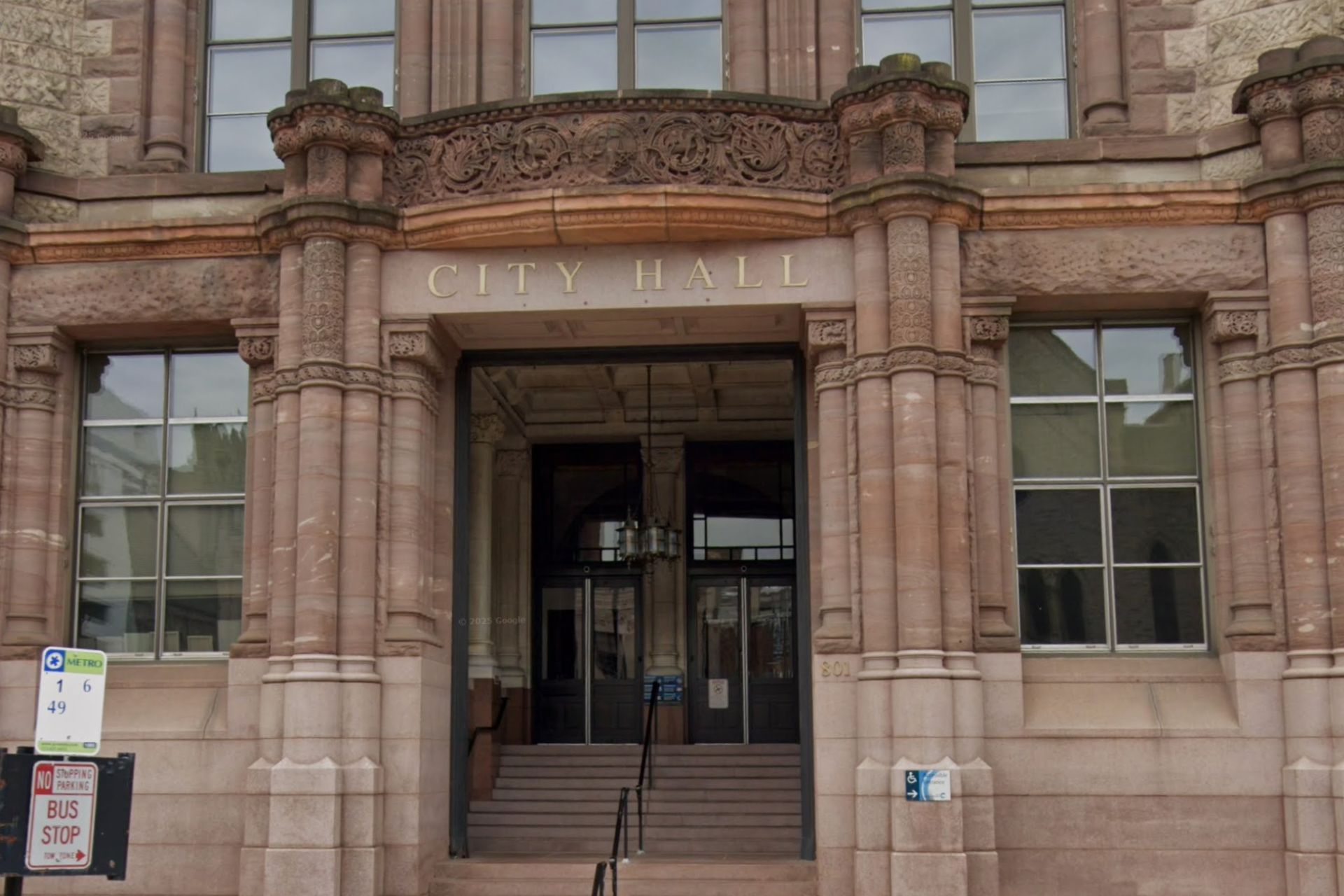 Front entrance of a historic stone building with ornate masonry, tall windows and a short flight of steps up to the doors.