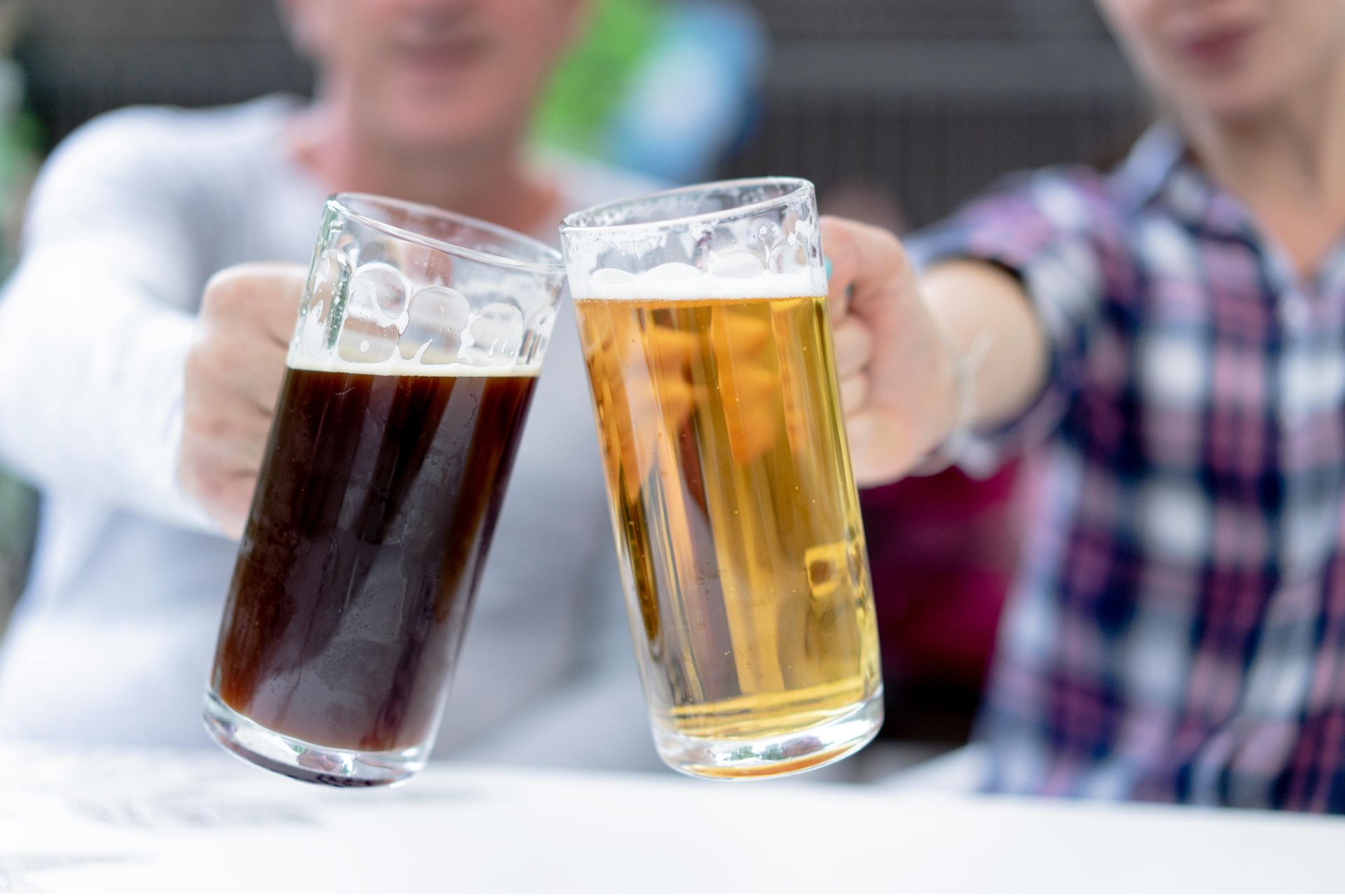 Two people clinking beer steins, one filled with dark beer and the other with golden lager