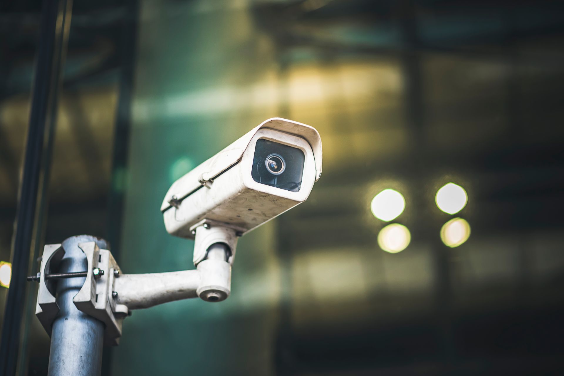 A white security camera mounted outdoors against a blurred background.