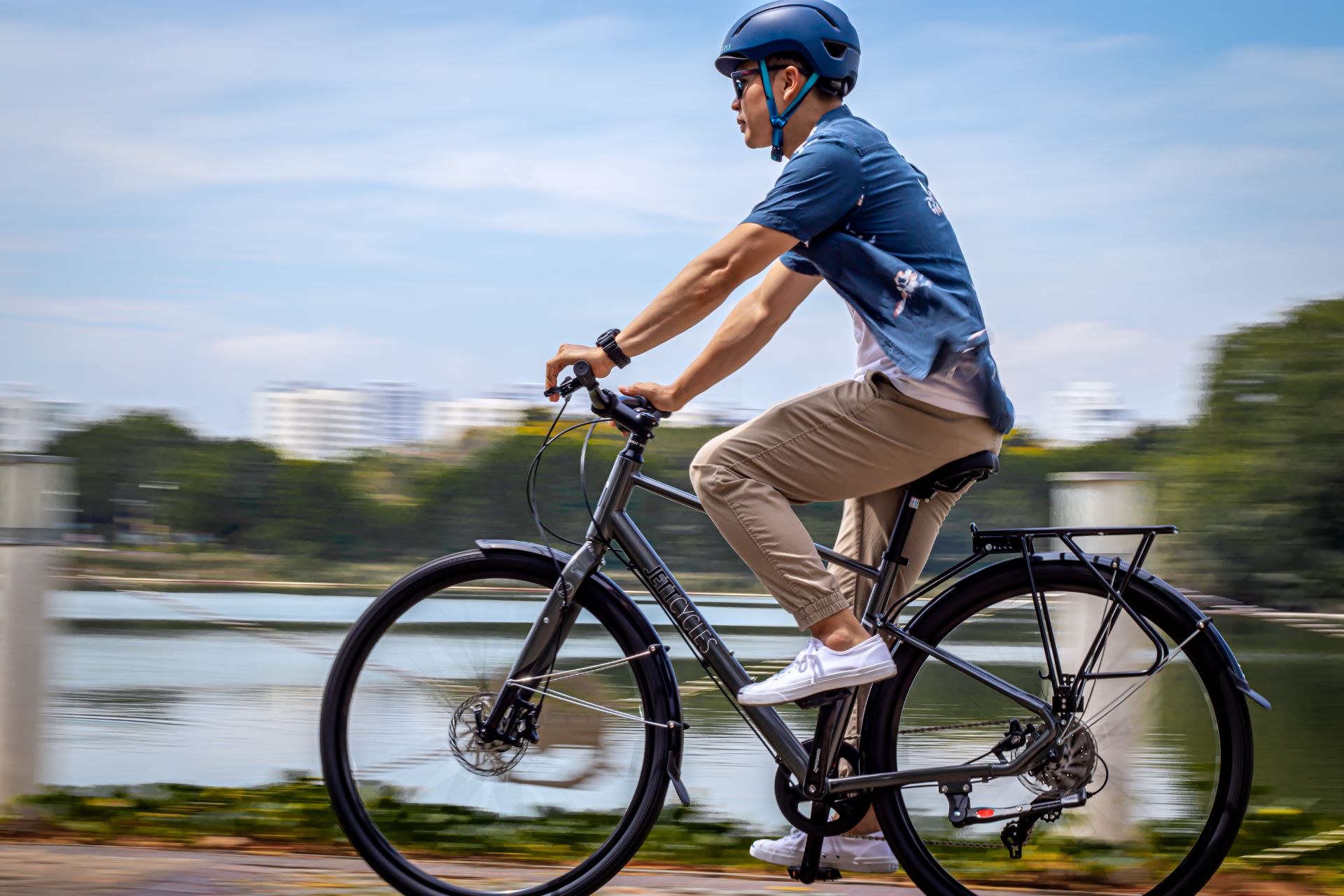 Cyclist in a blue shirt and helmet rides a bike along a waterfront path