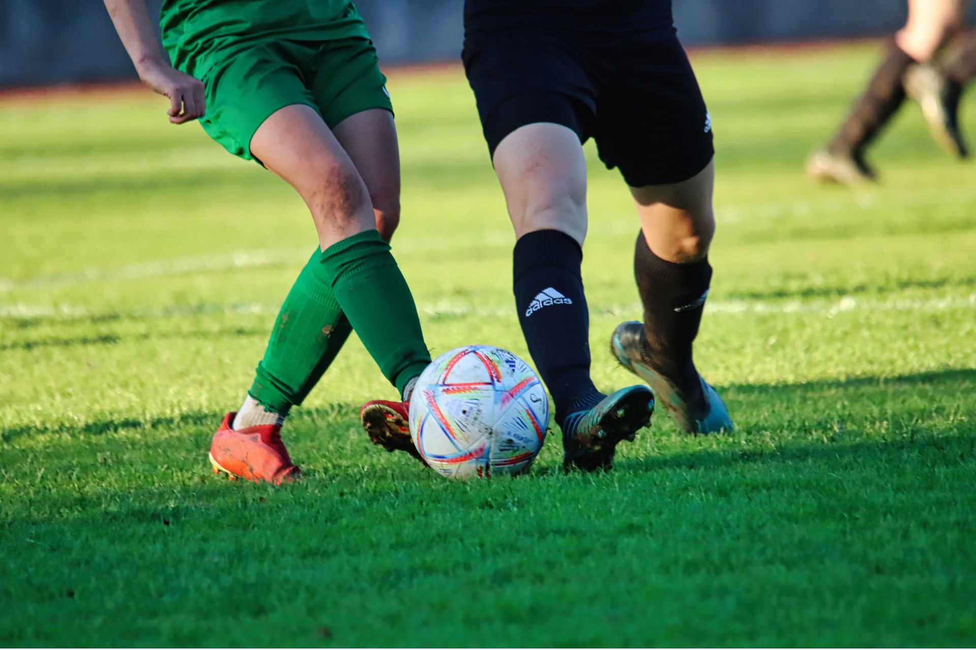 Two soccer players battling for possession of the ball on a green grass field.