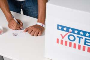 Person filling out a ballot at a table beside a “VOTE” sign