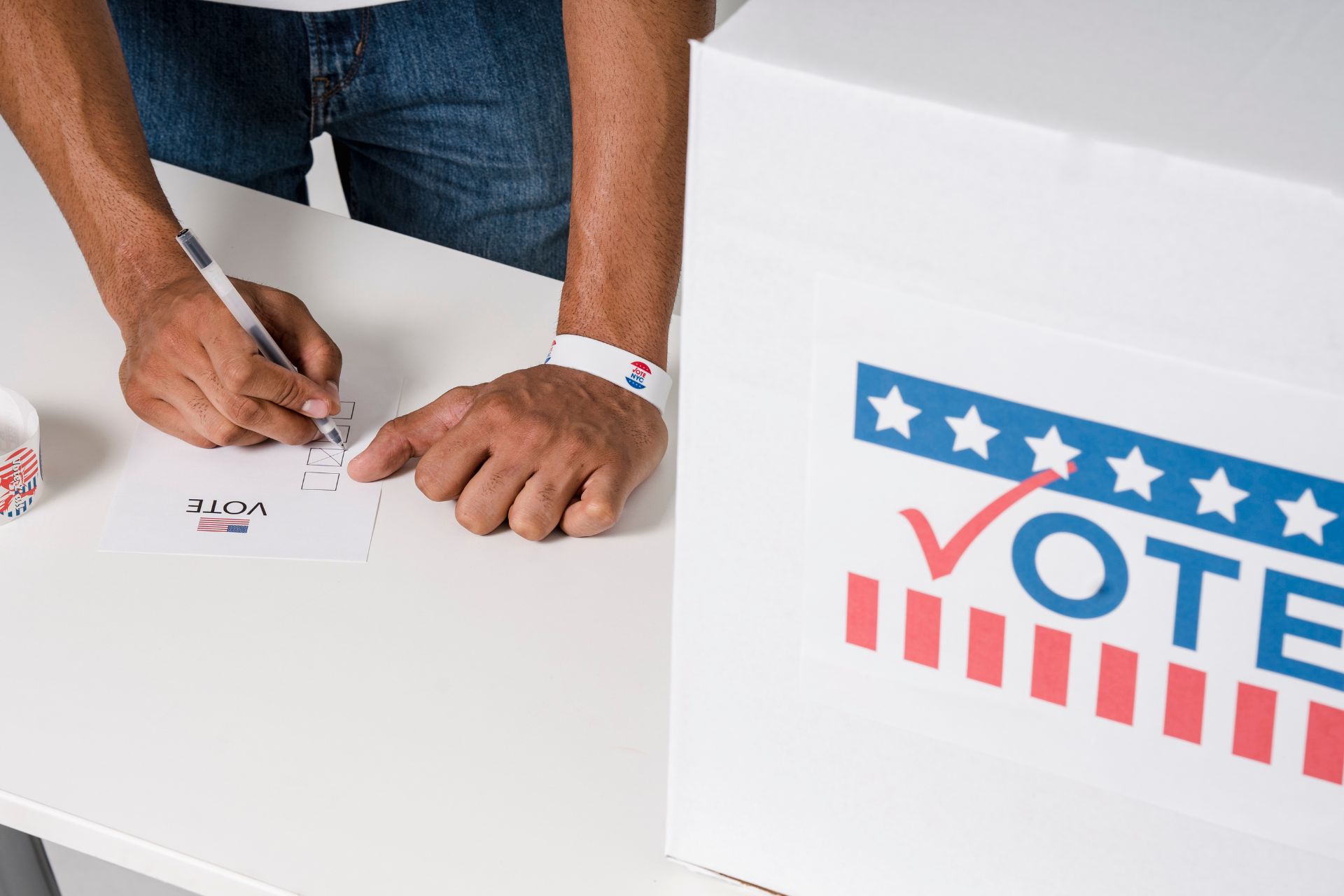 Person filling out a ballot at a table beside a “VOTE” sign