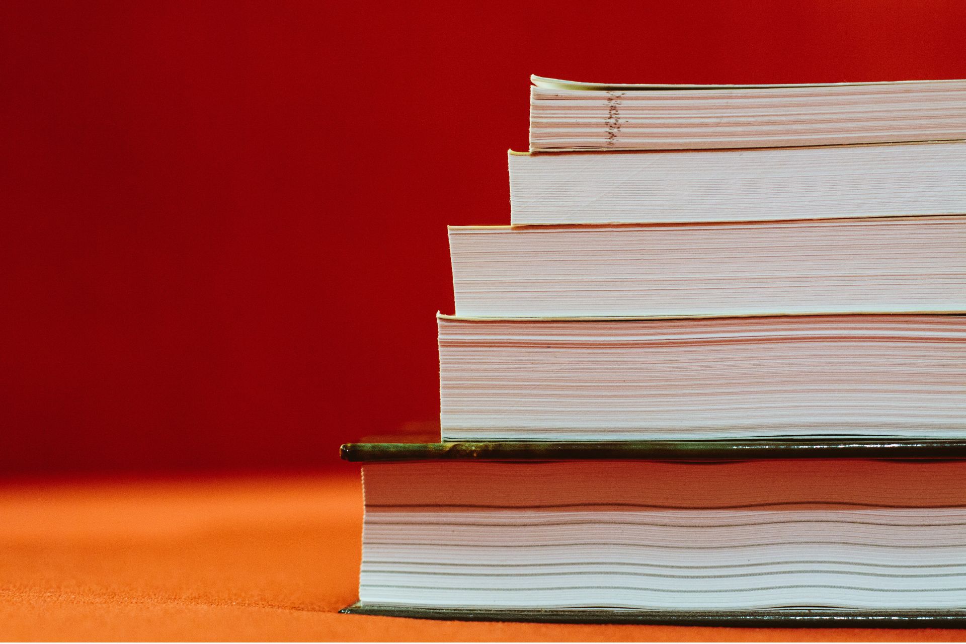 Stack of hardcover books on a wooden surface against a red background
