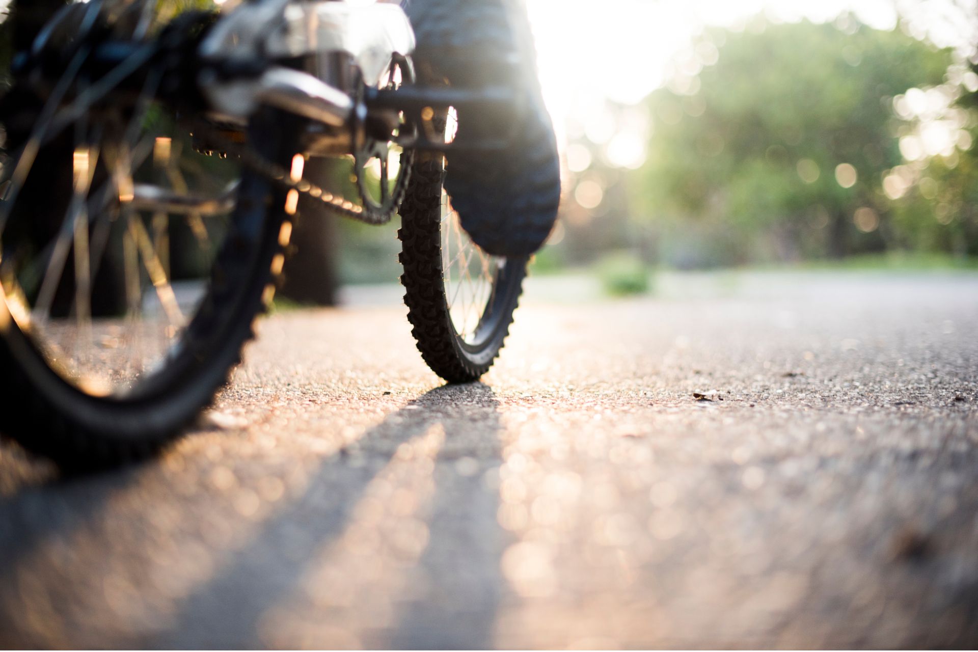 Close-up low-angle view of an e-bike's rear wheel and pedals on a paved path.