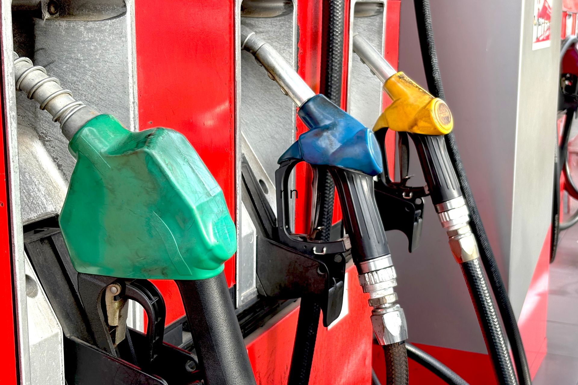 Close-up of green, blue, and yellow gas pump nozzles in their holsters at a gas station.