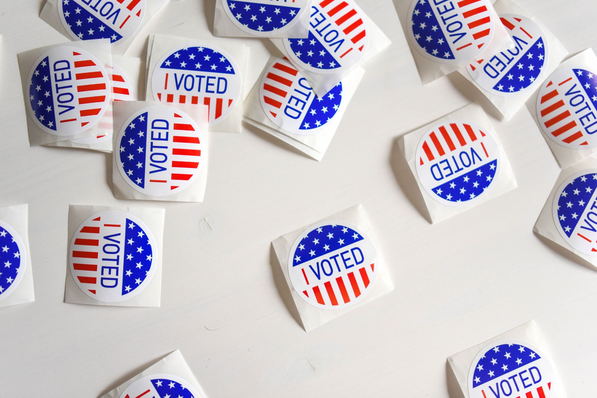 Several round “I Voted” stickers with red, white, and blue stars-and-stripes designs scattered on a light surface.